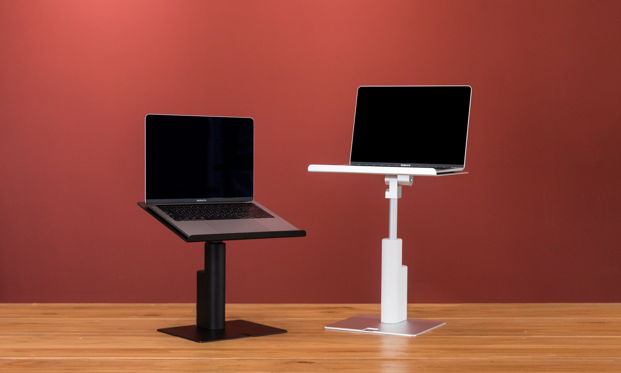maxtand e-power rising laptop stand in black and white on wooden tabletop and red wallpaper